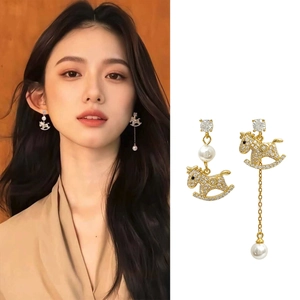 Detail of asymmetric gold plated pony earrings with pearls and zircon tassels on woman