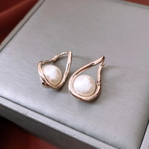 Macro shot of French gold-plated twisted pearl hoop earrings on a textured jewelry box