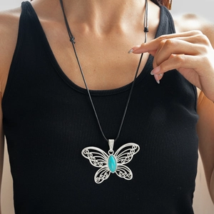 Detailed close-up of hollow butterfly pendant with turquoise stone on black wax cord