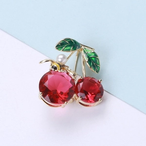 Detailed view of cherry brooch with red gemstones, green leaves and a small pearl bee