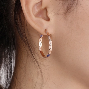 Close-up of rose gold titanium earrings featuring a textured twisted hoop design on model