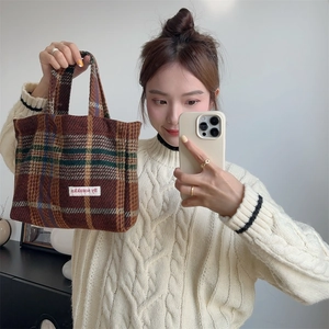 Detail of vintage brown plaid wool tote bag with white cloth label on a white sweater