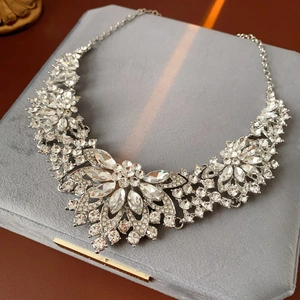 Detailed view of silver flower necklace set with sparkling crystals on velvet stand