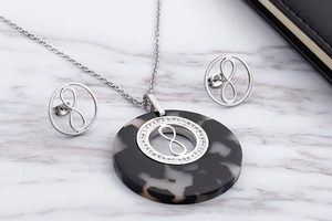 Detail view of tortoiseshell resin jewelry set with infinity charms on marble background