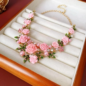 Détail de collier avec fleurs roses, feuilles vertes et perles dans un coffret à bijoux