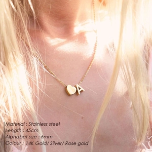 Close-up view of a personalized gold heart and initial pendant necklace on a female neck.