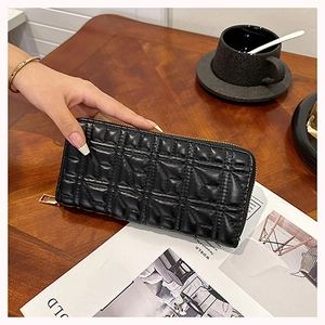 Detail shot of a black quilted long wallet held by hand on a table with a coffee cup