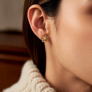 Close-up of golden hollow flower stud earrings with zircon centers on model ear