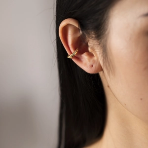Detailed close-up of a golden ear cuff with small zircons on a model's ear