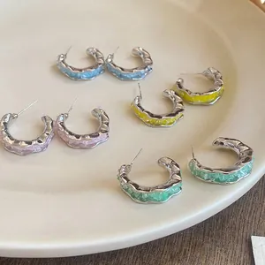 Détail de boucles d'oreilles créoles argentées avec résine colorée et texture métallique