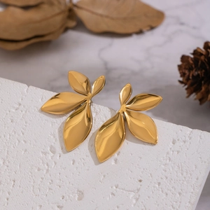 Elegant gold leaf-shaped stud earrings on white stone with artistic natural background