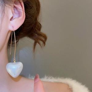Detail shot of heart-shaped pearl drop earrings worn on a gold hook with elegant finish