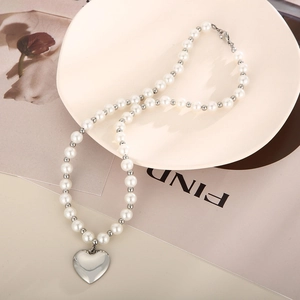 Gros plan d'un collier de perles avec pendentif cœur en argent sur une assiette blanche