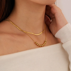 Close-up of double-layered gold flat snake chain and beaded necklace on a model's neck