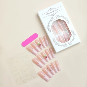 Detail view of pink gradient French fake nails with cherry rhinestones and tool kit