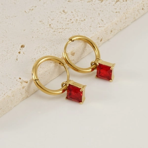 Détail de boucles d'oreilles créoles en acier doré avec zircon carré rouge étincelant