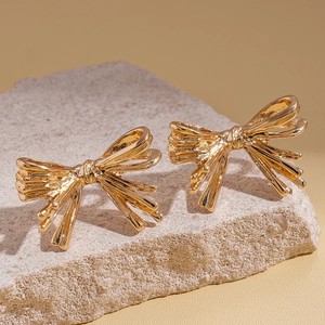 Detailed close-up of golden bow-shaped metal earrings on a textured stone surface