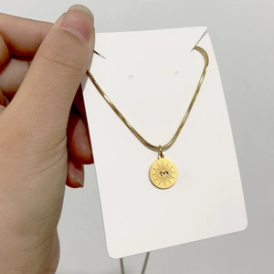 Detail of 18K gold snake chain necklace with engraved sun eye pendant on display card