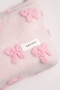 Detail of pink plush makeup bag featuring a 3D bow and H&R BAG brand label