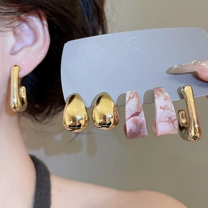 Close-up of three pairs of gold metal U-shaped, teardrop studs and marble resin hoop earrings