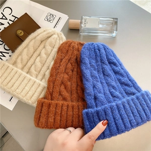 Flat lay of cable knit beanies in cream, caramel, and blue with stylish fashion accessories