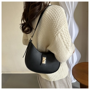 Close-up of black crescent shoulder bag with gold hardware on white knit sweater