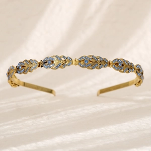 Close-up of golden leaf headband with blue rhinestones on a beige fabric background