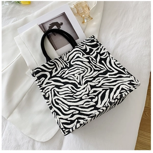 Flat lay of a zebra print canvas tote bag next to a glass and art magazine