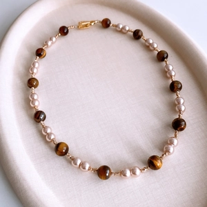 Close-up of tiger eye and pearl beaded necklace with gold lobster clasp on display tray