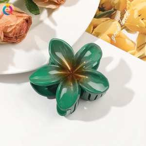Detail of vibrant green flower hair claw with gradient glitter on white tabletop