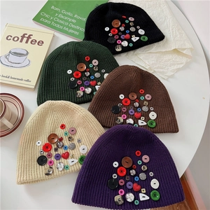 Flat lay of colorful button-decorated beanies in five colors on a white table