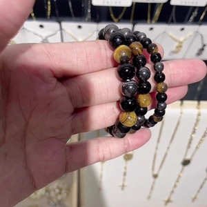 Three-piece beaded bracelet set featuring black and tiger eye natural stones held by hand