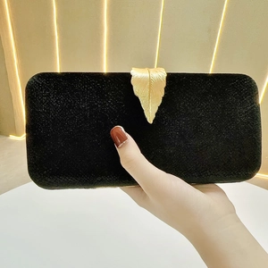Detail of velvet evening clutch with gold leaf clasp held by a hand against warm lights