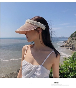 Detail of a handmade straw sun visor with pearl embellishments worn by a model seaside