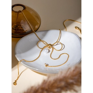 Detail of 18k gold plated bow necklace with white pearl and crystal drop on ceramic plate