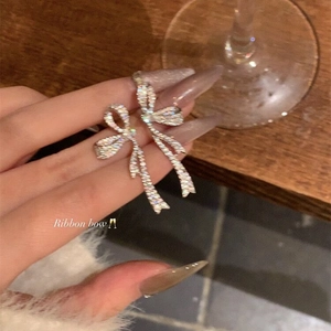 Close-up of elegant silver bow earrings with zircon stones held by a manicured hand