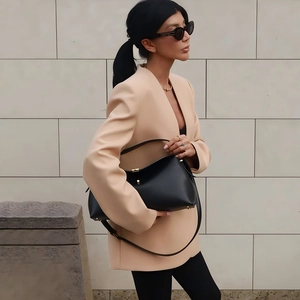 Detail of a chic beige collarless blazer paired with a black leather handbag