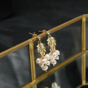 Macro shot of 18k gold plated leaf earrings with multiple freshwater pearls on glass