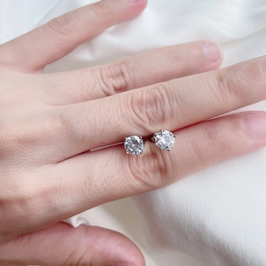 Macro shot of silver round-cut zircon stud earrings held in hand with classic four-prong setting