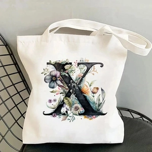 Close-up of white canvas tote bag with black floral letter X print on a chair