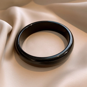 Polished black resin round bangle displayed on elegant champagne silk fabric