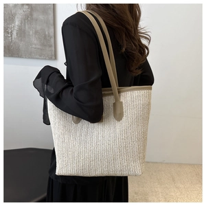 Close-up of beige woven tote bag with brown leather handles and twill texture details