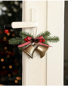 Nahaufnahme von Weihnachtsglocken mit rot gestreifter Schleife und Tannenzweigen an der Tür
