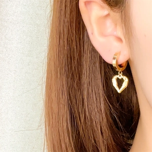 Close-up of a gold heart charm earring worn by a model in soft natural light