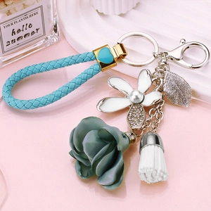 Close-up of floral keychain with blue woven strap, enamel flower, and white tassel charm