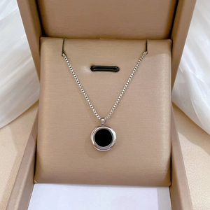 Detail of silver box chain necklace with black round pendant in a beige jewelry box
