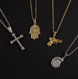 Detailed close-up of 24K gold plated Hamsa hand and cross pendants on black background
