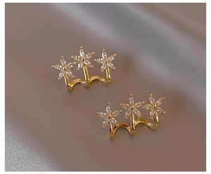 Detailed close-up of gold flower earrings with pavé crystals on grey satin fabric