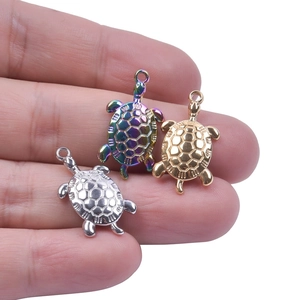 Detailed view of three sea turtle pendants in gold, silver, and rainbow finishes on a finger