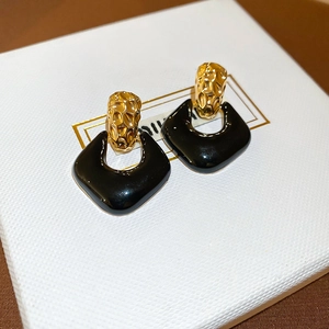 Close-up of geometric earrings with gold hammered texture and black enamel shield pendant
